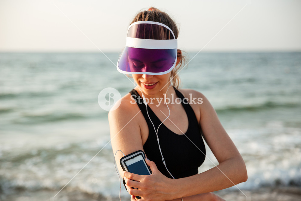 Fitness runner woman resting on beach with phone case sport armband strap