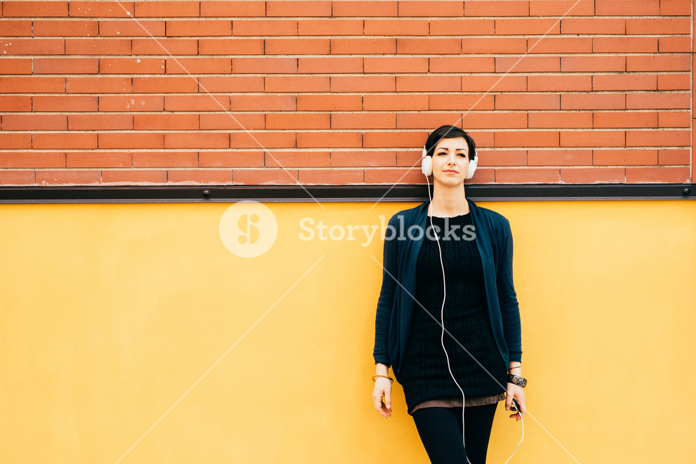 Serene woman enjoying music with headphones and smartphone, dancing against a wall