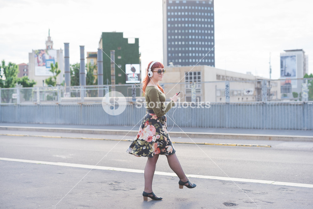Young woman enjoying music and dancing in the city, radiating joy and carefree vibes - wearing green shirt, floral skirt