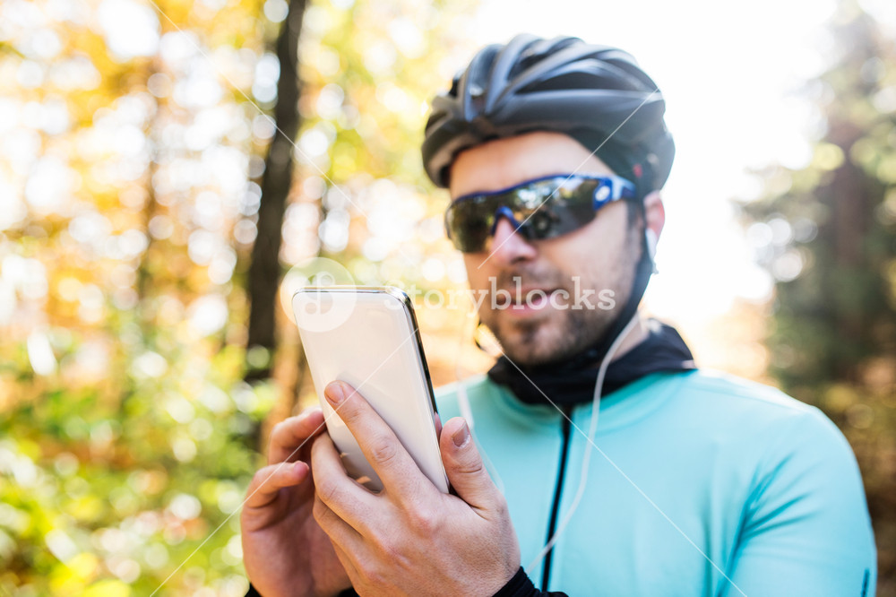 Young man cycling in sunny autumn nature, enjoying music on his phone.