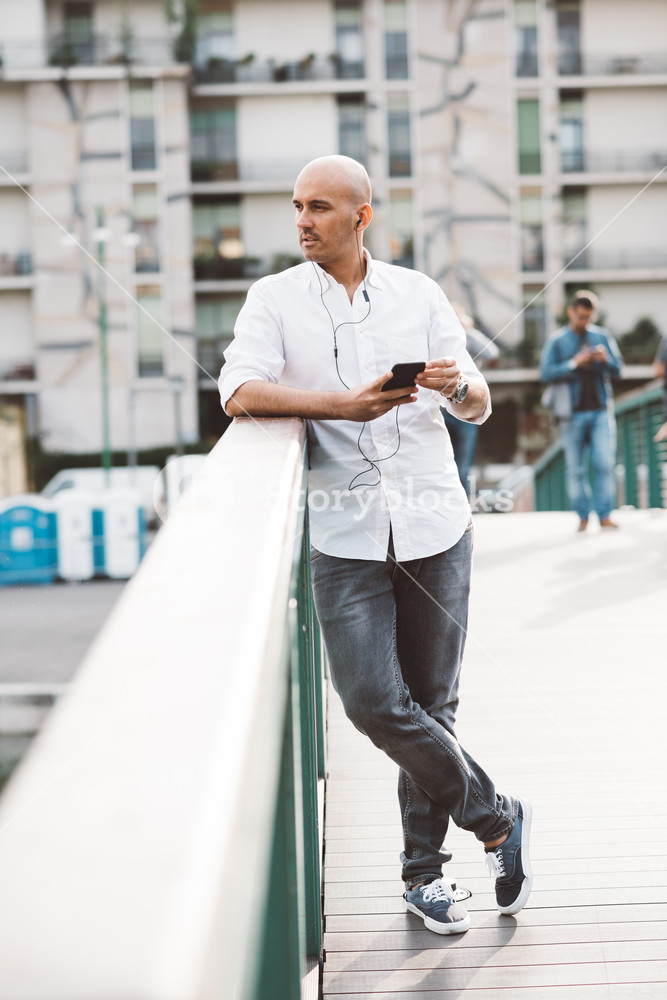 Young man listening to music with earphones and smartphone outdoors in the city - audio, playlist, relaxing concept
