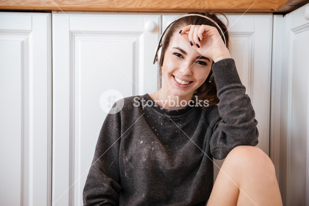 Woman enjoying music in kitchen at home, looking at camera