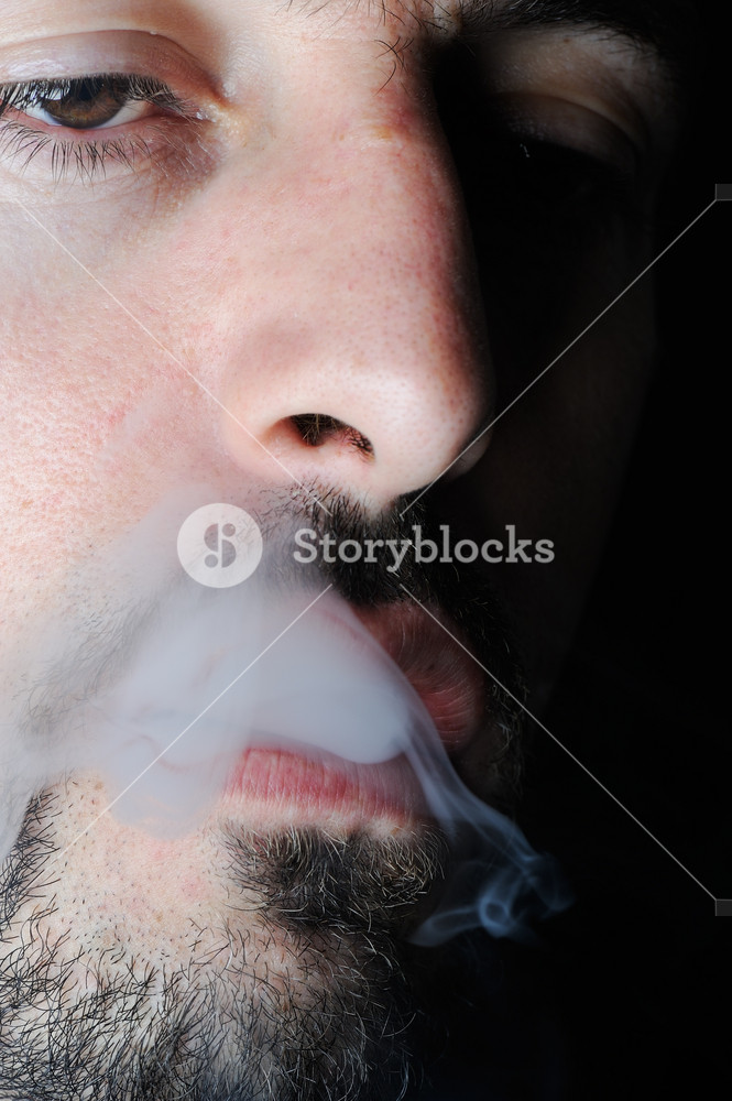 Man in dark exhaling cigarette smoke Royalty-Free Stock Photo SBI-300996386 
