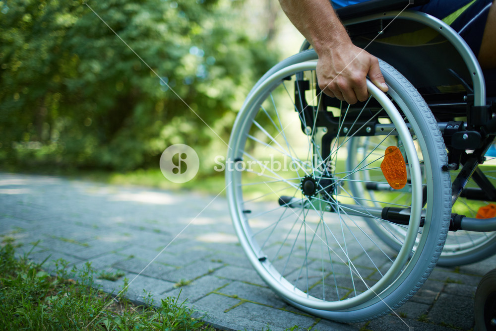 Close-up of male hand on wheel of wheelchair during walk in park ...