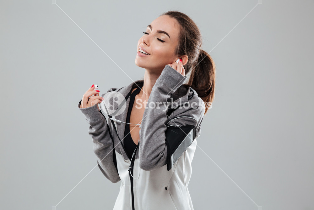 Pleased sports woman listening music with closed eyes over gray background
