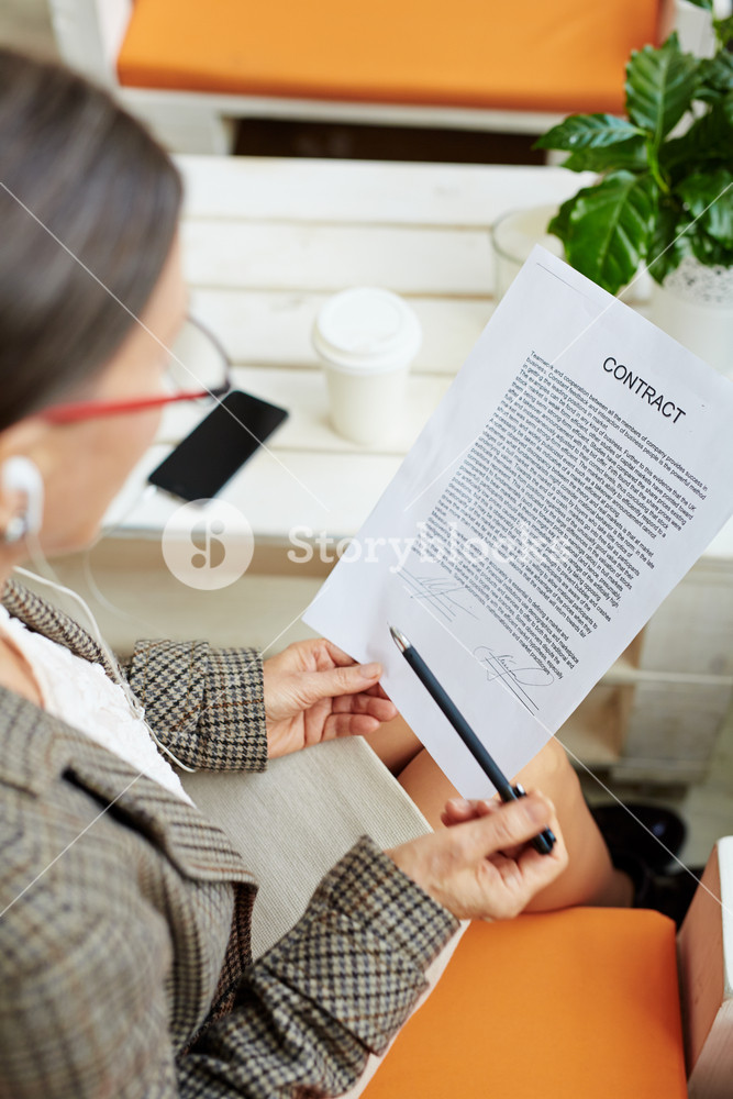 Profile view of senior woman with business contract in hands enjoying music at a cafe