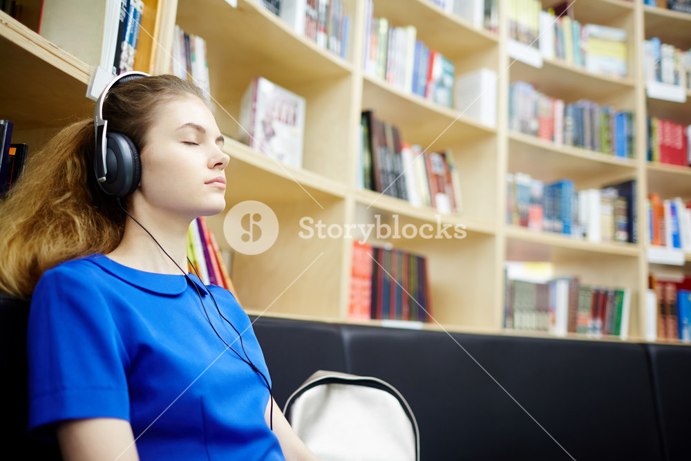 Side view portrait of young woman enjoying audiobook with headphones in modern library