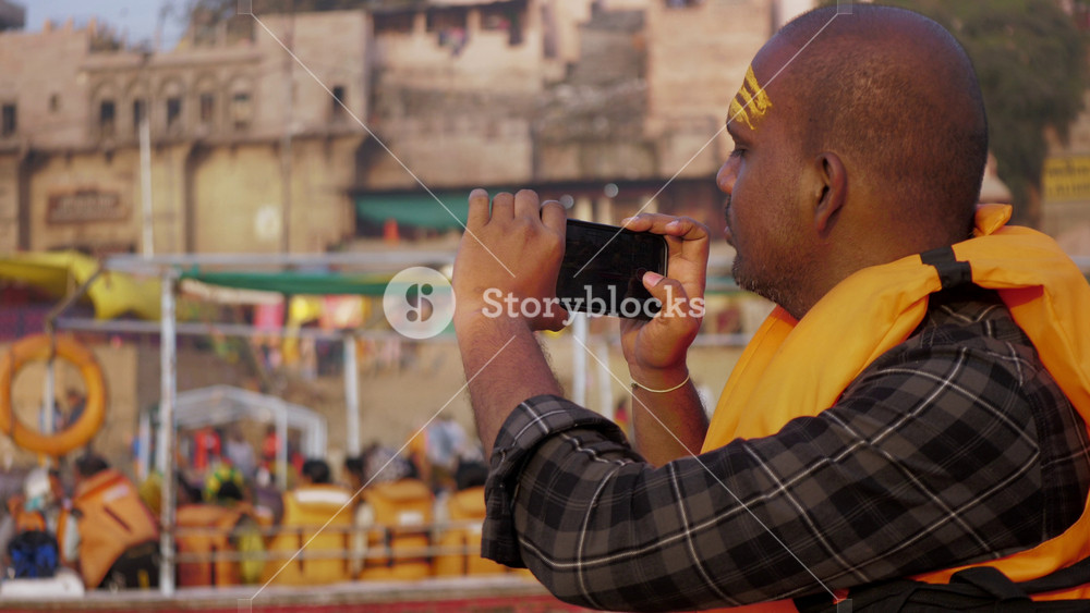 Varanasi, Uttar Pradesh, India - November 2 2025: A bald male Hindu devotee clicking pictures of the the holy Ganges river and ancient ghats of Banaras city on a mobile phone or smartphone camera