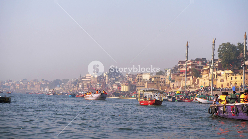 Varanasi, Uttar Pradesh, India - November 2 2025: A daylight shot of the multiple wooden boats carrying tourists and devotees on the holy river Ganges with ancient ghats of Banaras in the background