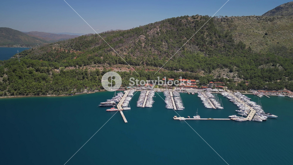 Turquoise waters of Turkey's coast meet luxury yachts. Orhaniye marina seen from above in Turkiye. Aerial view of boats and forested slopes.