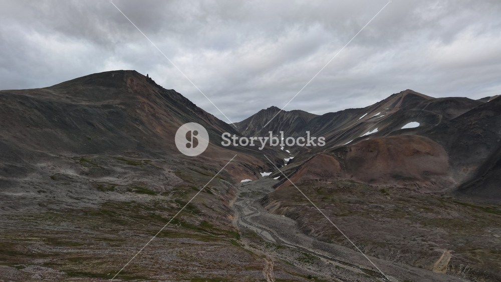 Wide mountain basin under heavy clouds in Russia, Chukotka, Provideniya. Aerial establishing shot slowly pans across tundra ridges, snow