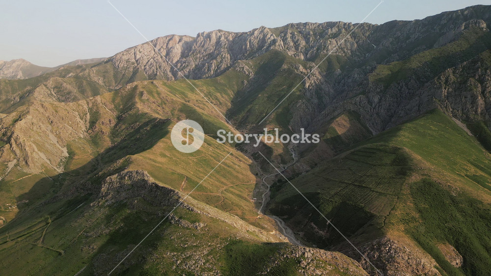 Golden hour panorama of grassy hills and rocky escarpment in the Boysun area of Surkhandarya. Drone perspective follows the valley line
