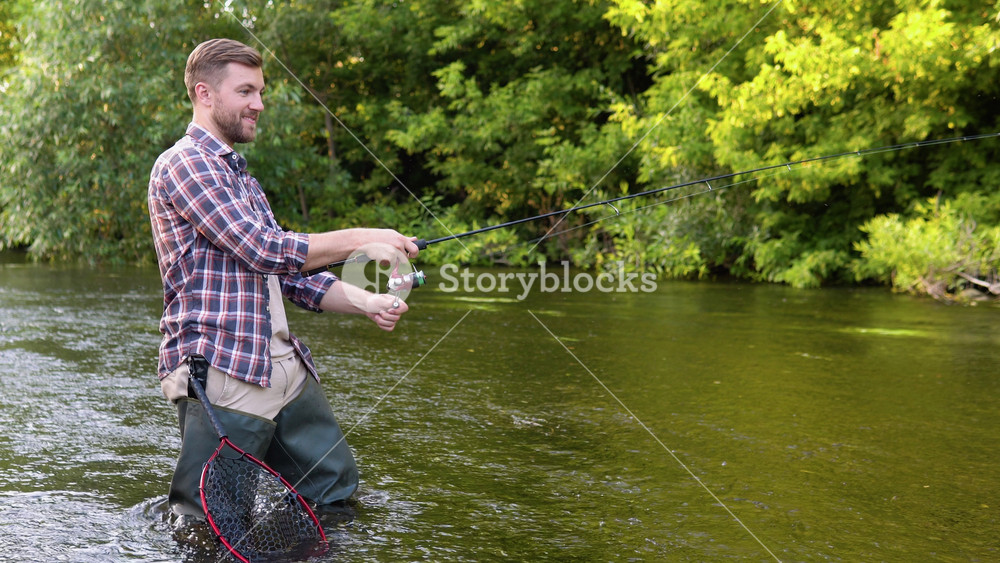 A fisherman throws a fishing rod standing knee-deep in the water of the river. Fly fishing for trout. Summer holidays and people concept