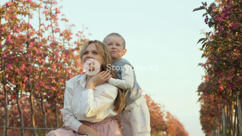 Mom and son hugging on the street in the garden near the young trees with pink flowers. A little gentleman. Love between parents and