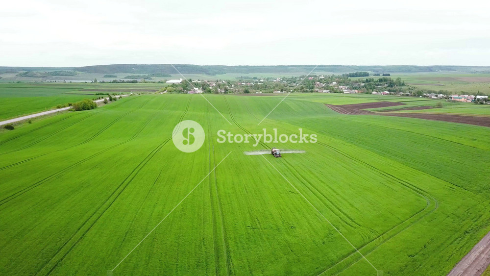 Aerial view of farming tractor spraying on field with sprayer, herbicides and pesticides. Tractor is spraying pesticides on grain field