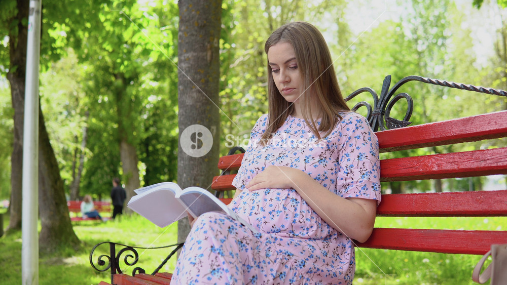 Pregnant woman in a summer dress with a floral print walks in the park. A pregnant woman on a park bench reads a book for expectant mothers