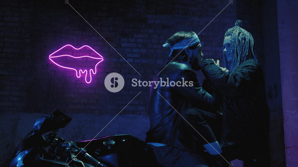 A girl in love and a guy are sitting on a super sport motorcycle flirting and hugging against the background of a neon sign