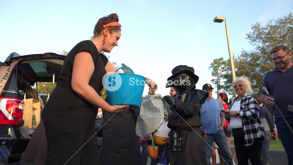 Orlando, Florida, USA - 10. 30. 2024: A community volunteer shares candy from a blue bucket with a child wearing a plague doctor costume