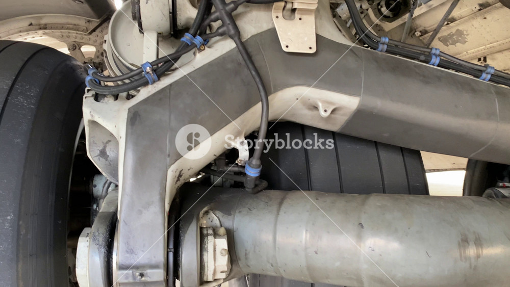 Detailed view of an aircraft landing gear wheel with hydraulic lines and structural supports. Large tires and metal components show aviation