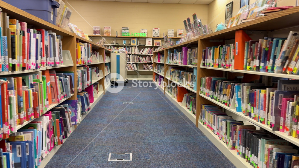 Orlando, Florida, USA - 06. 11. 2024: A long aisle in a school library is lined with shelves of organized books. Bright labels and signs mark