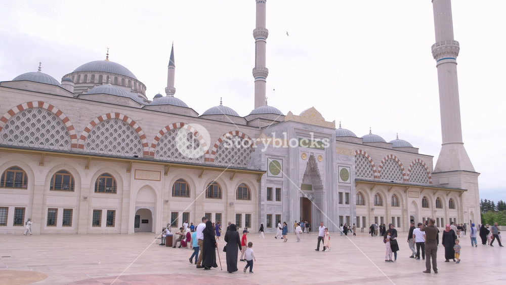 Istanbul, Turkey - 06. 29. 2023: Spacious mosque courtyard with families, children, and visitors walking near the entrance of a grand Islamic