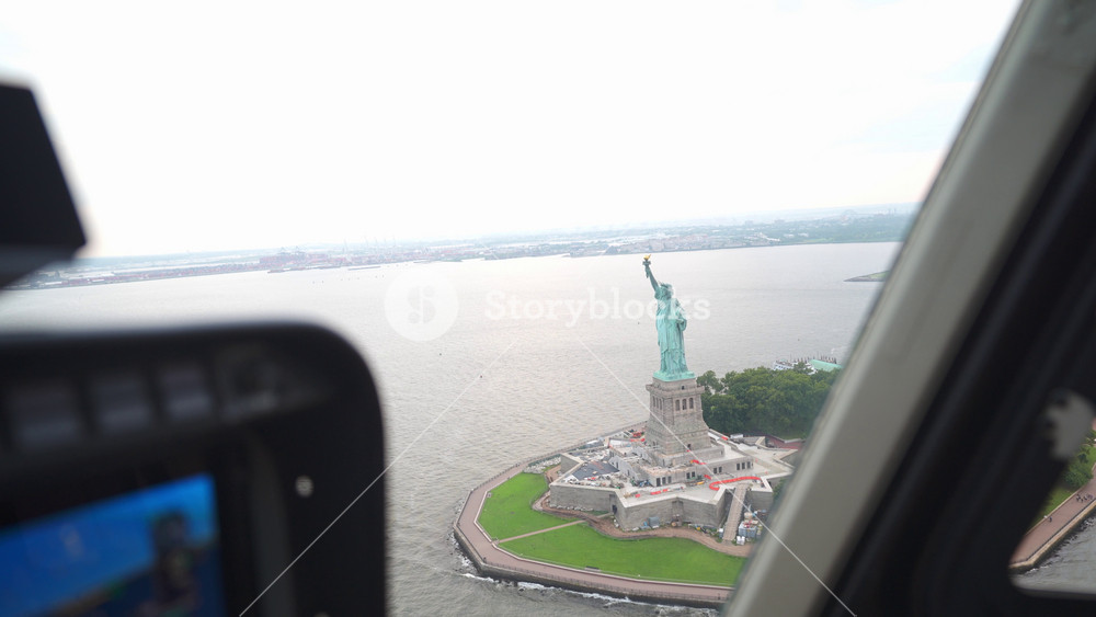 Aerial view of the Statue of Liberty photographed from inside a helicopter over New York Harbor. The iconic monument stands proudly on