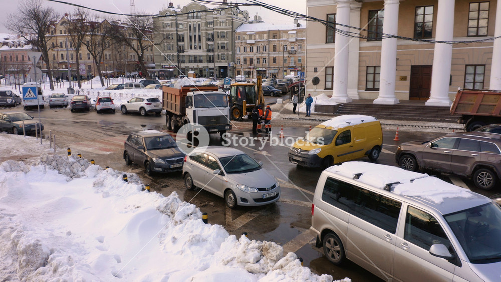 City center cars traffic on a winter day. Municipal service removing snow from the city road. Urban landscape with transport and city