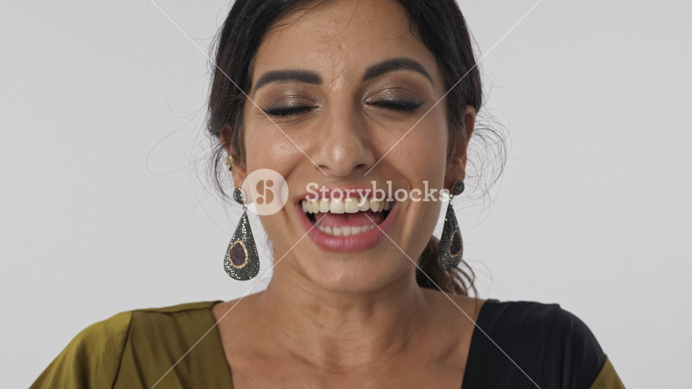 Close up view of Cheerful pretty hindu woman in traditional dress rejoicing and looking at the camera over grey background