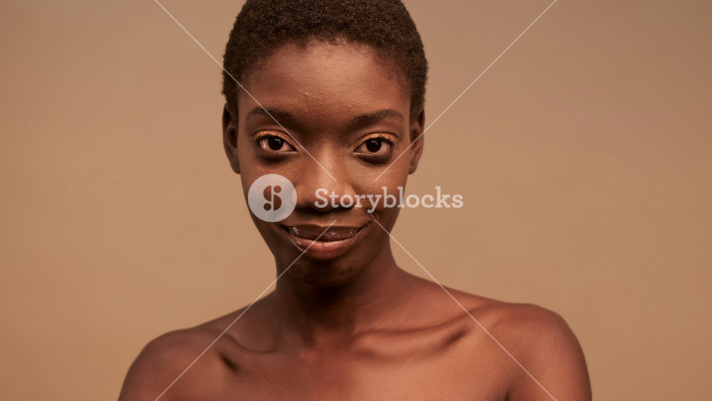 Close up view of Happy pretty african woman with short black hair posing and looking at the camera over beige background