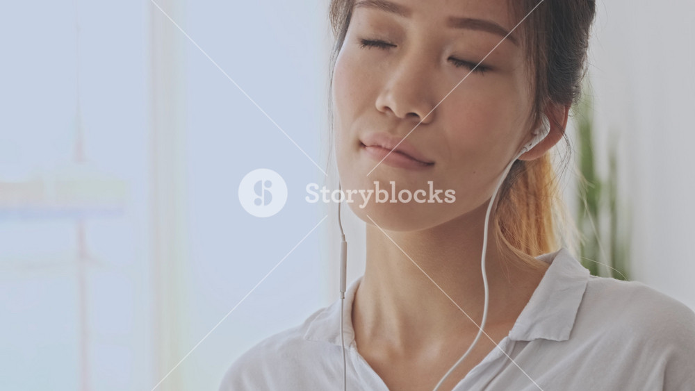 Crop view of asian young woman enjoy listening to music with closed eyes using wired headphones in the white office