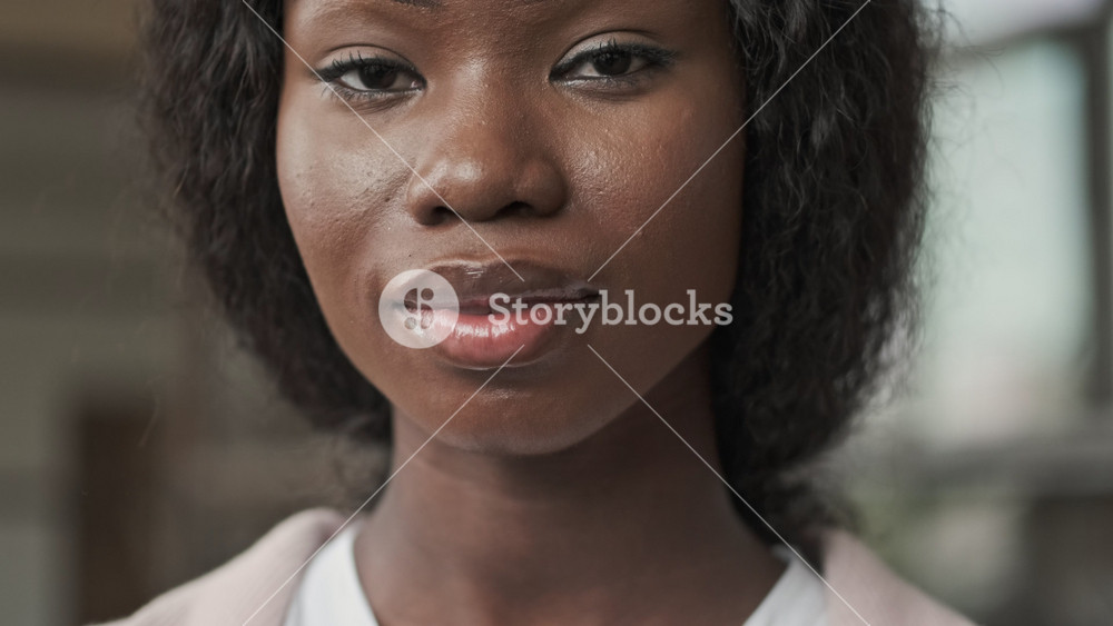A close-up view of a young african american businesswoman is opening her eyes and looking to the camera standing in the office