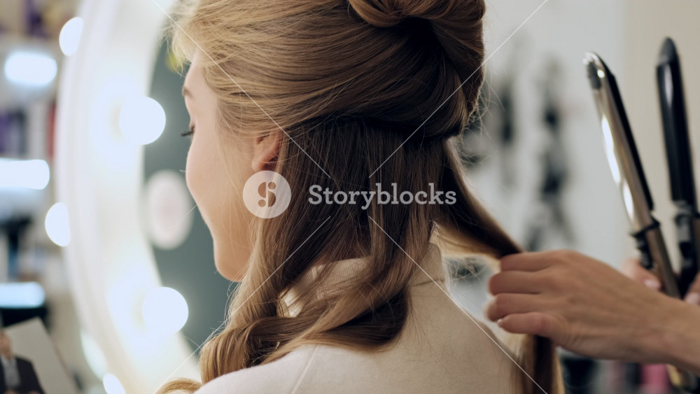 A close up view of a professional hairdresser is doing curls to a client with blonde hair in a beauty salon