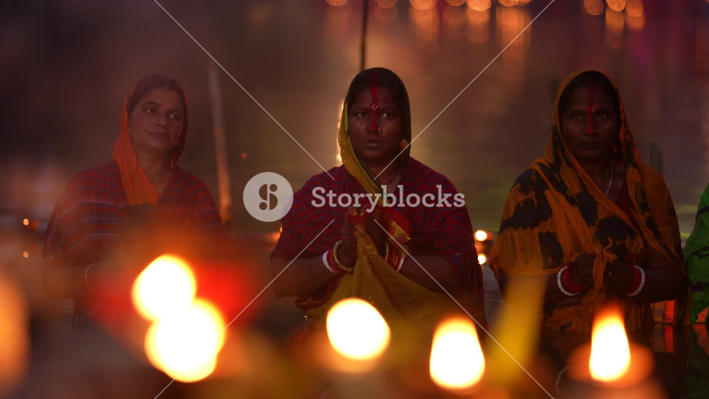 Bogura, Bangladesh - 20 December 2023: View of Hindu women in traditional sarees performing religious rituals in the water during a festival with blurred lights in the foreground.