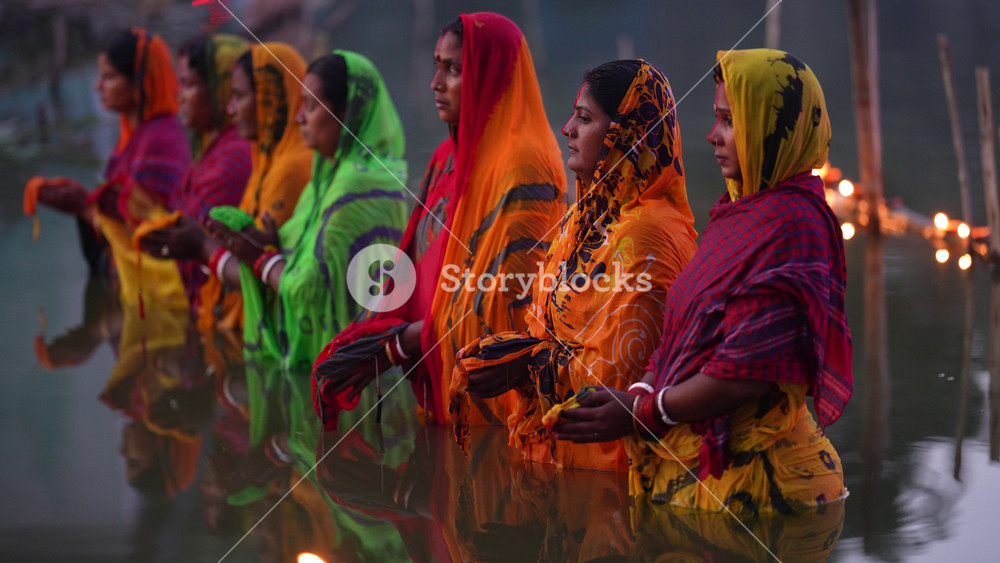 Bogura, Bangladesh - 20 December 2023: View of Hindu women standing in a river wearing colorful saris while performing a religious ritual during sunset.