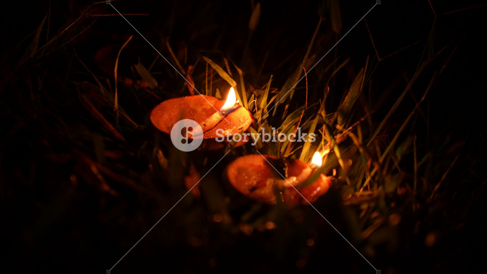 Bogura, Bangladesh - 20 December 2023: View of traditional oil lamps burning in the grass at night with a warm glow illuminating the surrounding greenery.