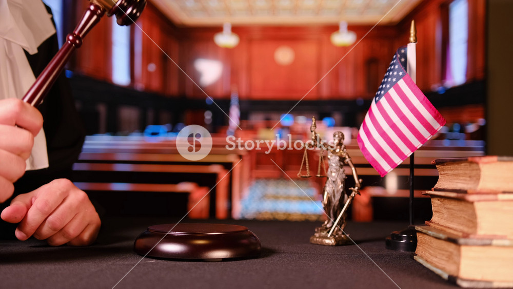 Gavel, American flag, and justice statue on desk inside courtroom. Symbol of law, democracy, and justice in the United States.