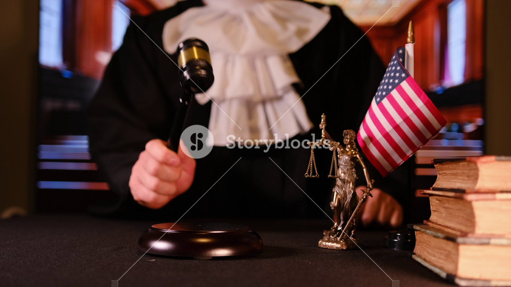 Judge hand striking gavel on desk with law books and statue of justice nearby. Concept of decision, order, and legal authority.