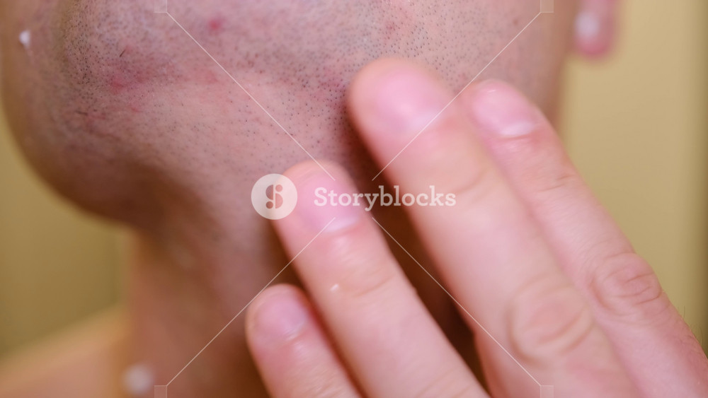 Close-up macro footage of man shaving his face with razor blade, showing detailed skin and hair texture. Concept of male grooming and