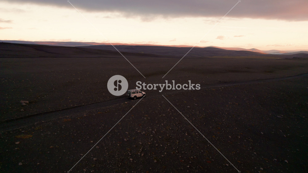 Epic Iceland Sunrise 4 Wheel Drive White Car Drives Offroad F-Road. Drone Follows Behind Vehicle Over Dirt Wide Martian Landscape Adventure Destination in Icelandic Highlands.