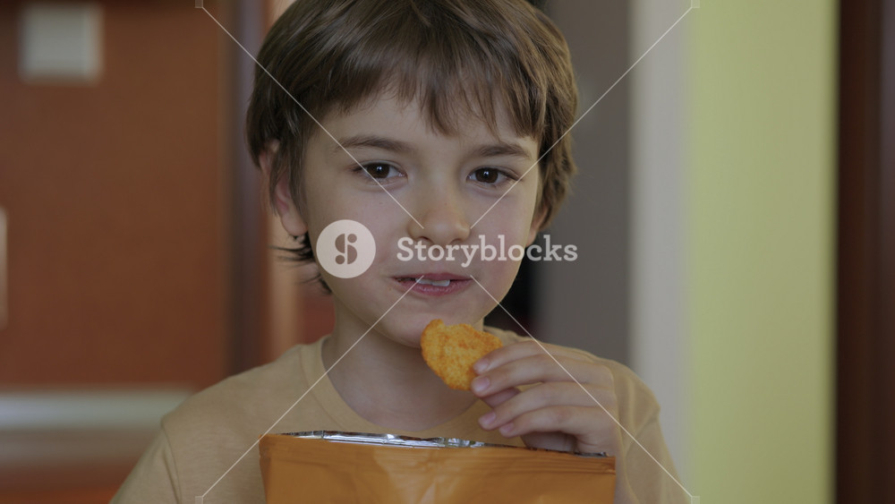 Hungry Boy Enjoying Tasty Chips. Kid Eating Unhealthy Potatoes Crisps. Snack on Junk Food. Portrait of Boy With Satisfied Face. Child Happily Eats Fast Food, Junk Food at Home. Childhood Obesity.