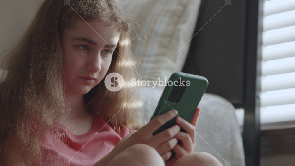 Teenage girl with serious expression using smartphone at home. Young girl with concerned look scrolls on her mobile phone. Cyberbullying, teen mental health, social media issues, youth isolation.
