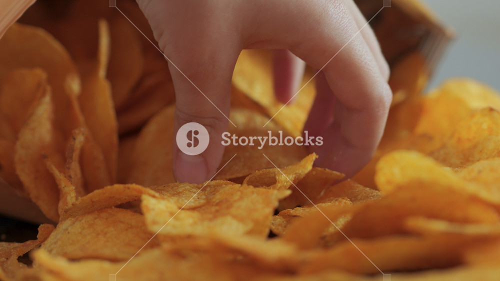 Close-up Potato Chips In Open Package. Potatoes Chips. Person Hands Take Potato Chips From Pack on Wood Table. Eating Fast Food, Junk Food at Home. Childhood Obesity. High Calorie Food.