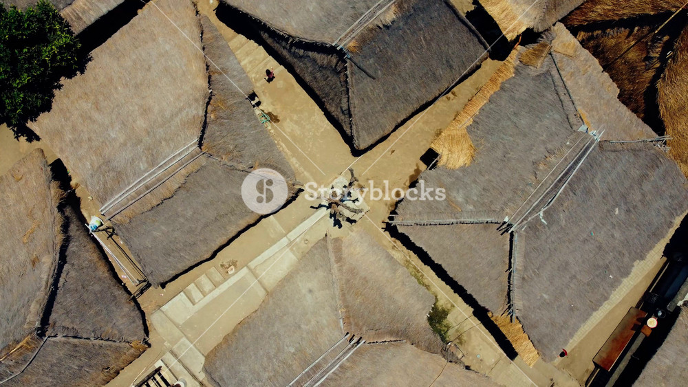 An aerial view of the densely populated Sade Village in Lombok reveals lush farmlands and traditional homes under the bright midday sun, showcasing vibrant community life.