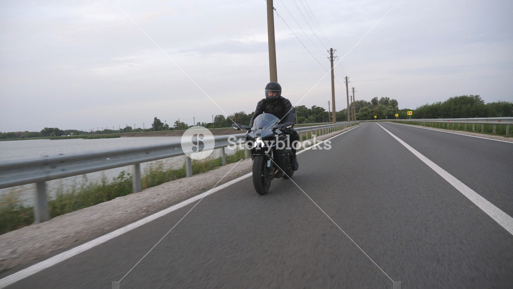 Motorcyclist races his motorcycle on country road. Young man in helmet rides on modern sport motorbike at rural route. Guy driving bike during trip. Concept of travel and freedom. Slow motion.