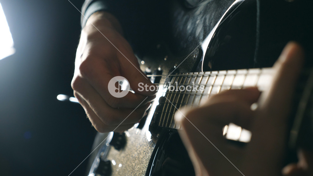 Hands of male musician playing at electric guitar. Mens arms plays solo of rock music. Close up fingers of guitarist at the strings. Beautiful black background at studio. Slow motion Close up.