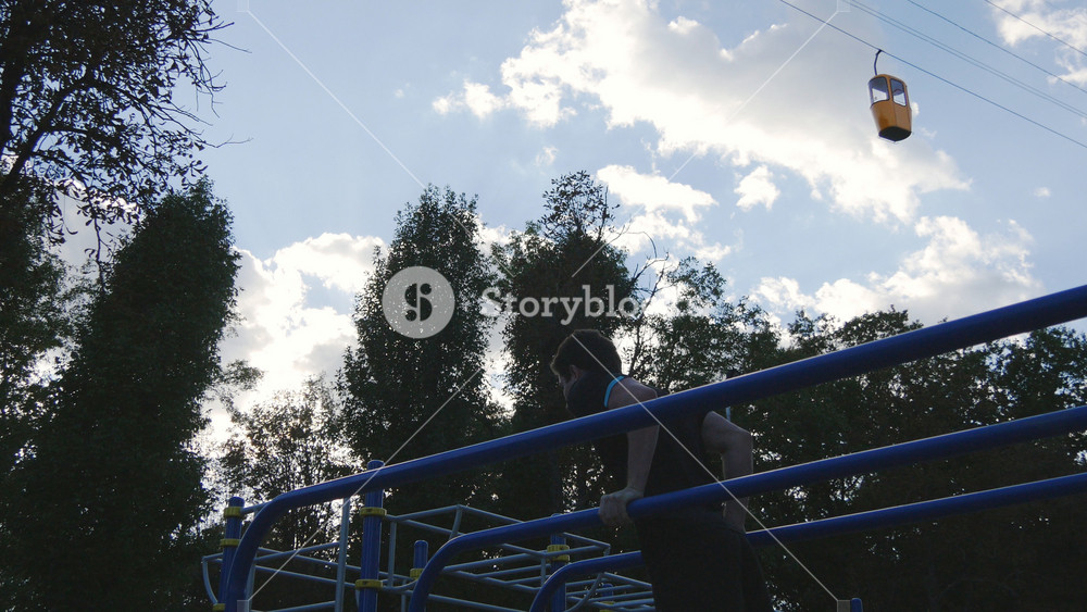 Athletic man doing push ups on parallel bars at sports ground in city park. Strong young muscular guy training outdoor in summer. Athlete exercising at playground. Workout healthy lifestyle. Closeup.