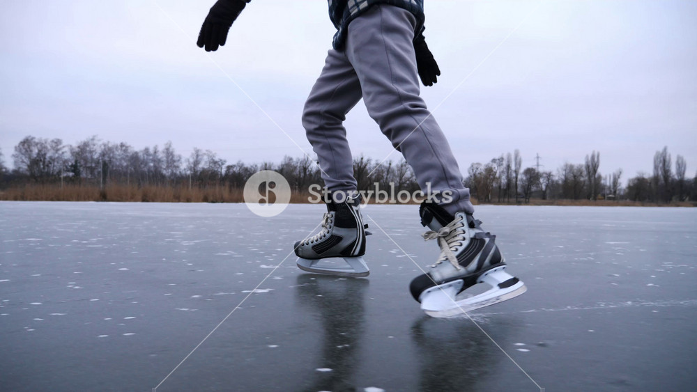 Male skater skating on frozen river at cloudy winter day. Young guy shod in figure skates sliding on ice rink outdoor. Sportsman training at lake in cold weather. Active leisure at wintertime. Slow mo.