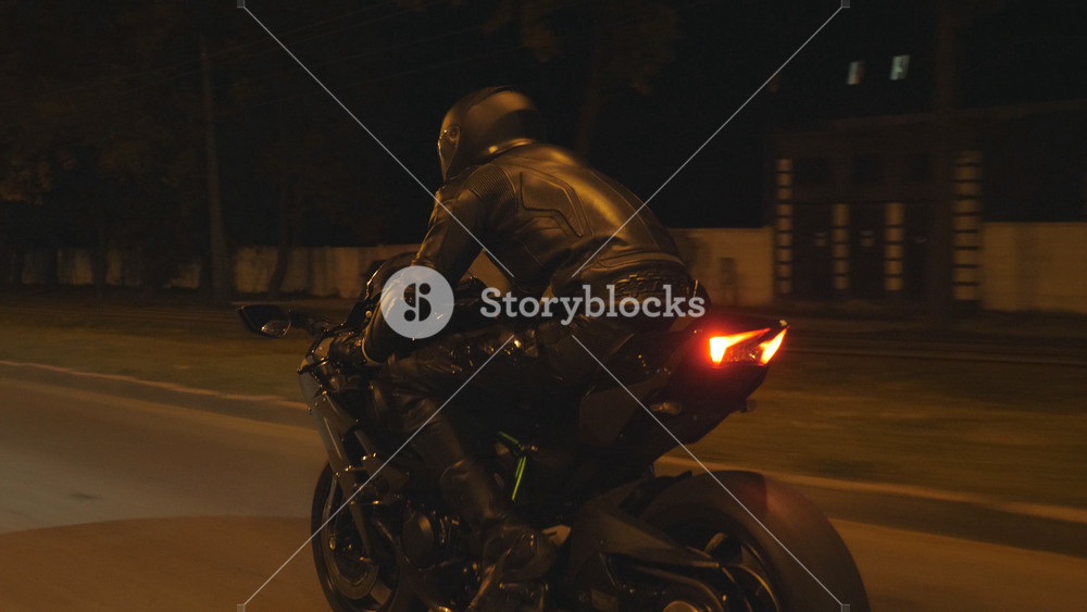 Motorcyclist racing his motorcycle on evening city. Man riding on modern sport motorbike at night street of town. Guy driving bike during trip. Concept of freedom and adventure. Rear view Close up