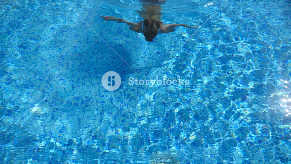 Woman swim under the water and emerges on the surface. Young beautiful girl swimming in pool. Summer vacation or holiday concept. Slow motion