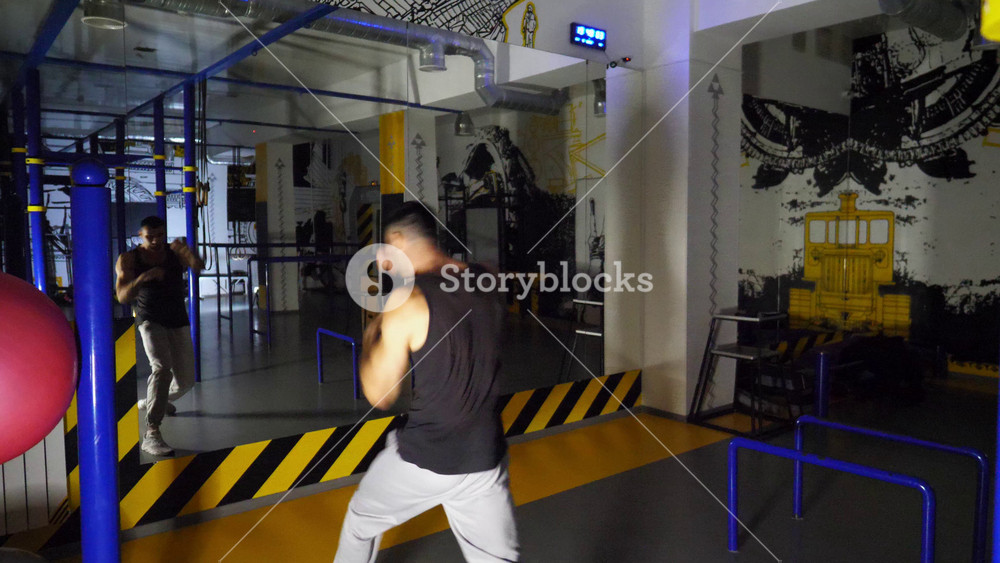 Strong sporty man practicing shadow boxing at sport club. Young muscular athlete demonstrating punches the air at modern gym. Male kickboxer training at fitness centre. Concept of healthy lifestyle.